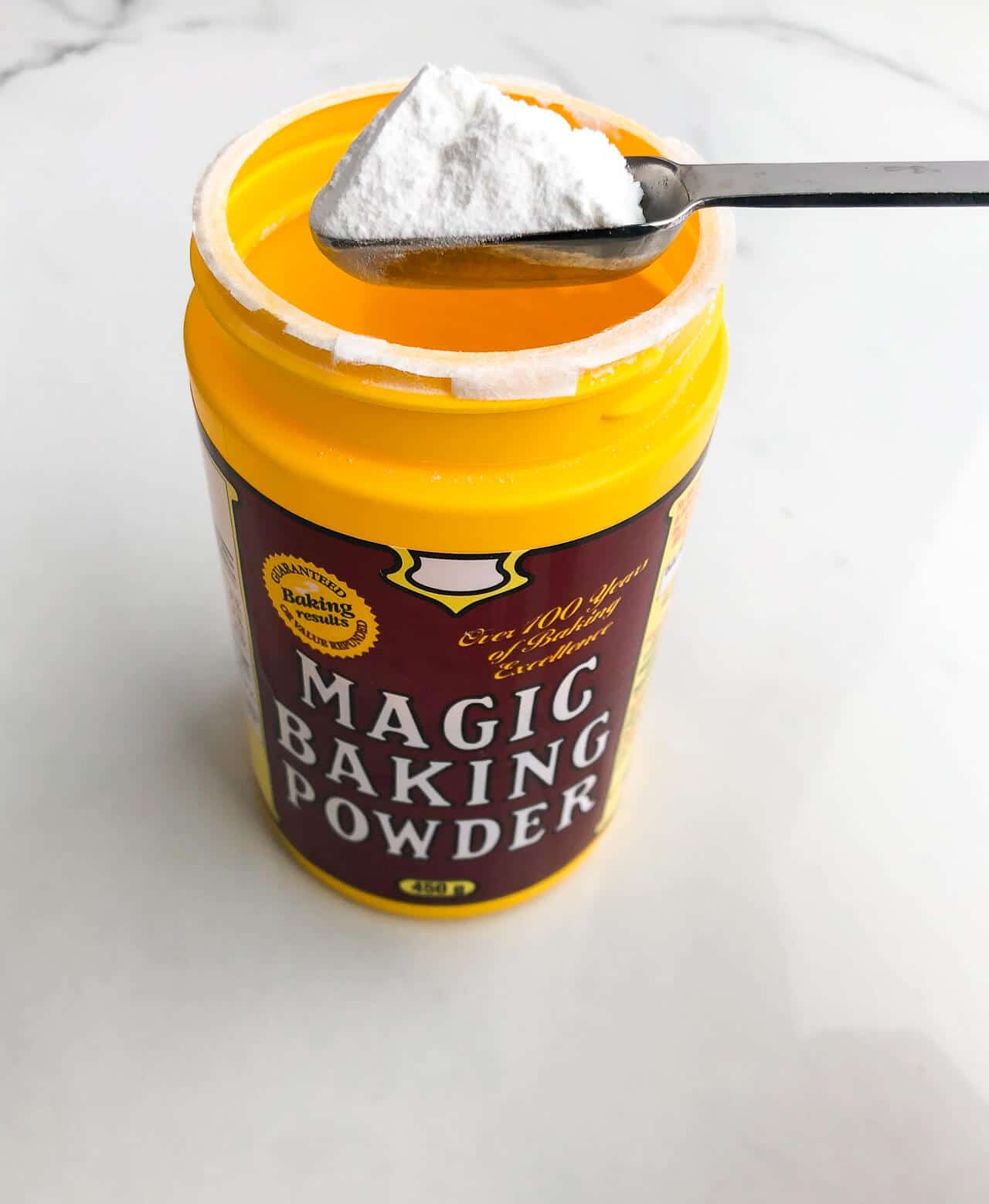 a yellow plastic container of Magic baking powder with 1 teaspoon scooped
