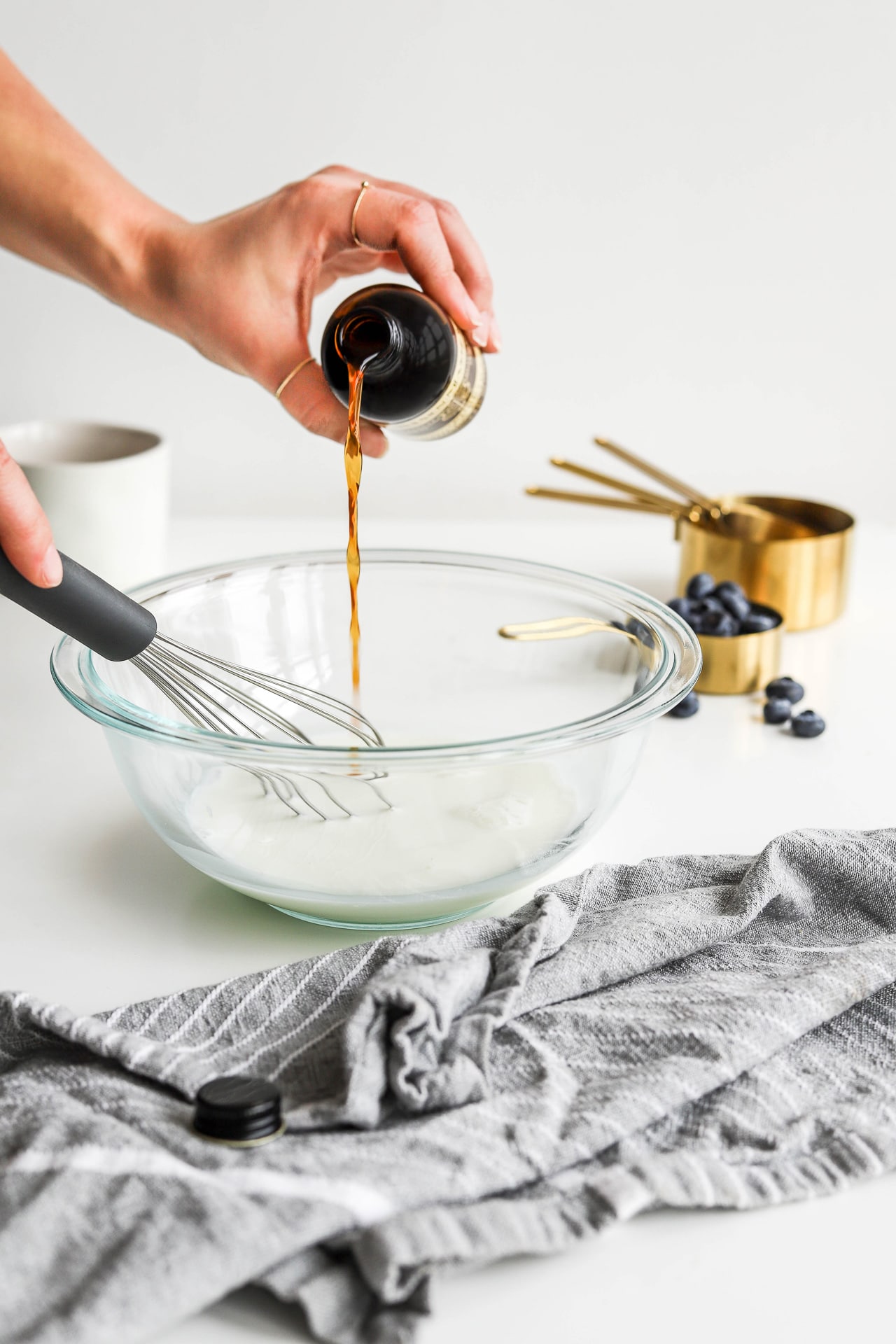 Pouring vanilla into cake batter in a glass bowl with grey linen
