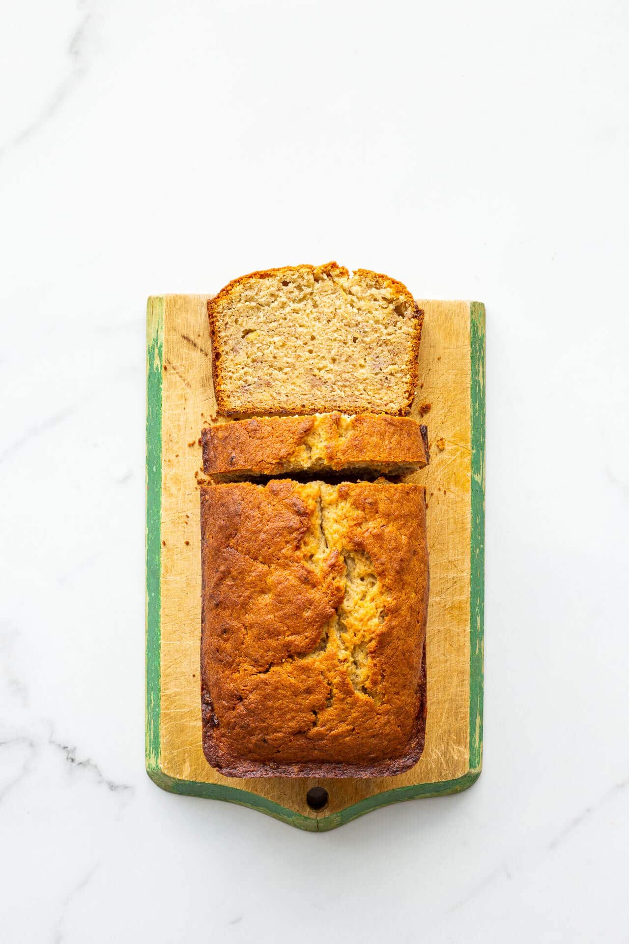 Golden brown banana bread on a vintage wood cutting board with painted green trim.
