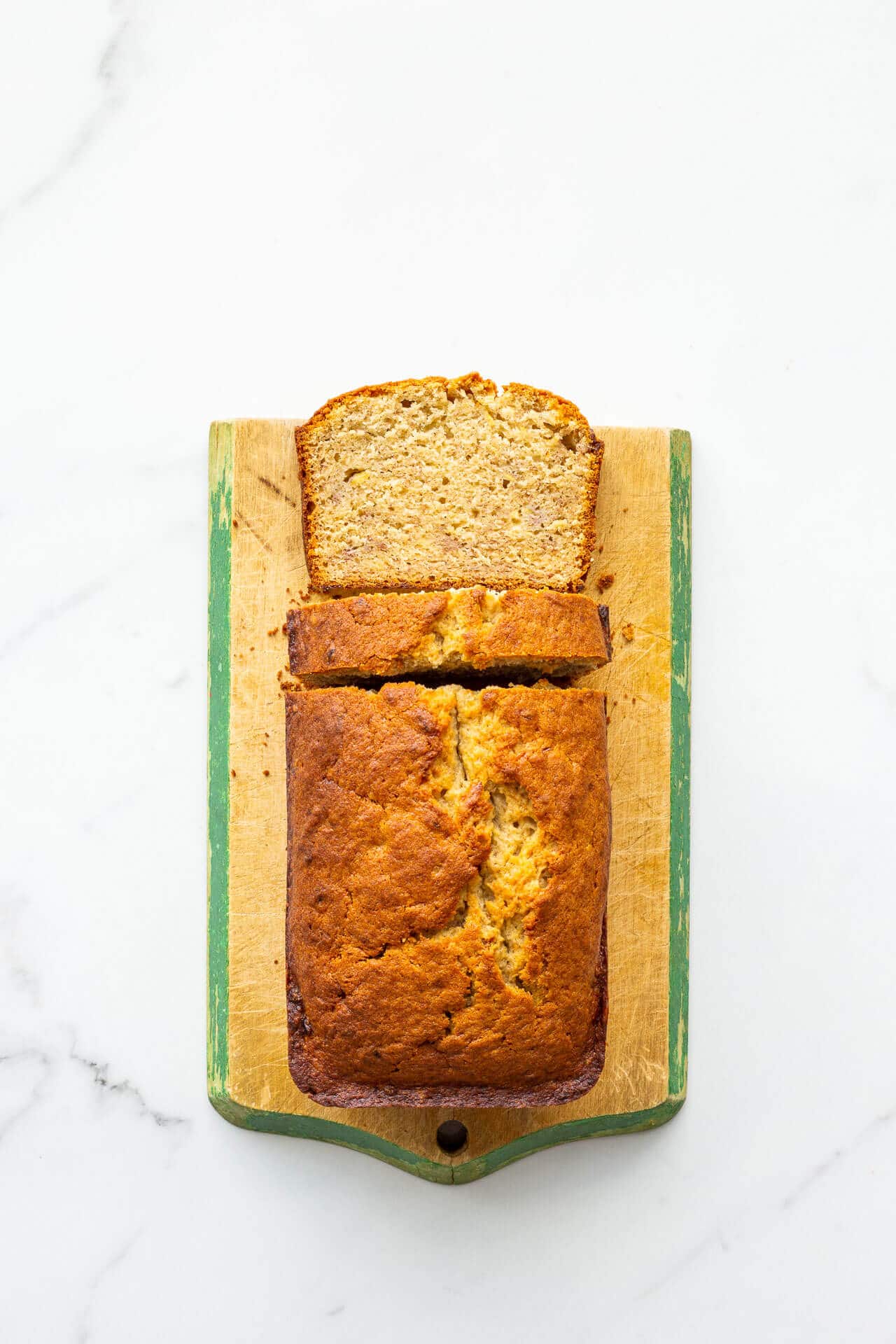 Golden brown banana bread on a vintage wood cutting board with painted green trim