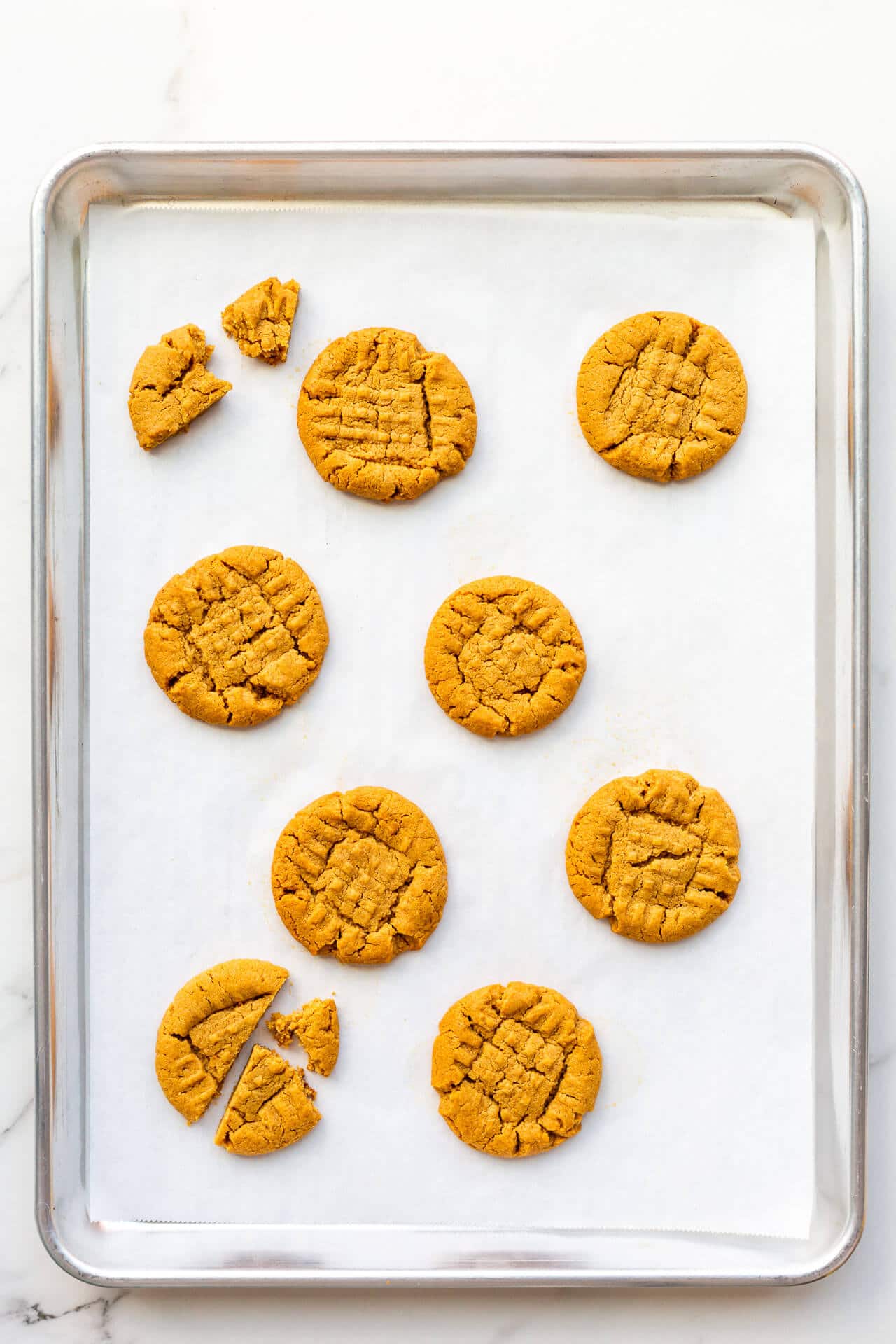 Baked flourless peanut butter cookies on a sheet pan lined with parchment with signature criss cross pattern