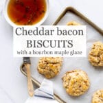 Bacon biscuits are brushed with a bourbon maple glaze infused with fresh thyme using a pastry brush as they cool on a parchment lined sheet pan with a white and blue striped towel