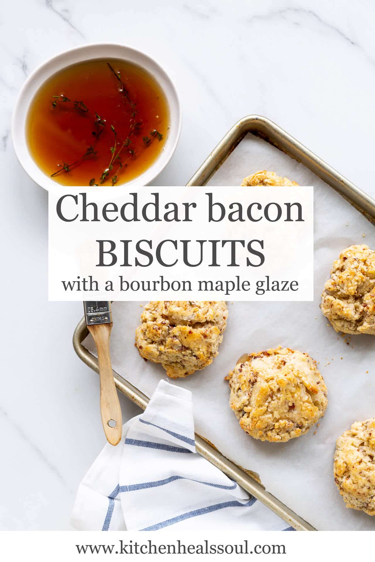 Bacon biscuits are brushed with a bourbon maple glaze infused with fresh thyme using a pastry brush as they cool on a parchment lined sheet pan with a white and blue striped towel