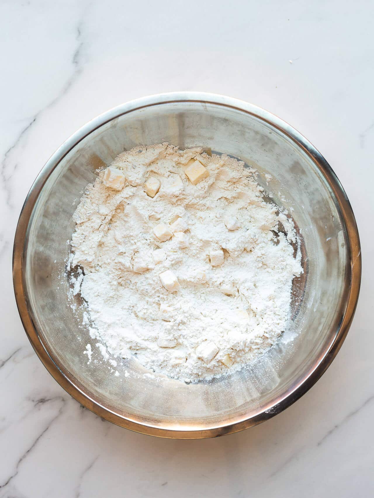 Incorporating cubes of butter into dry ingredients in a metal mixing bowl to make scones