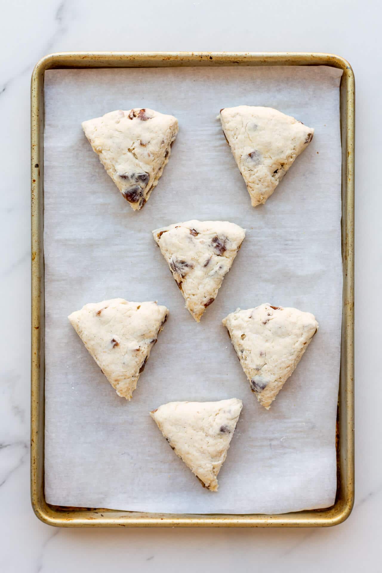 Six (6) triangle wedge scones on a parchment-lined sheet pan before baking