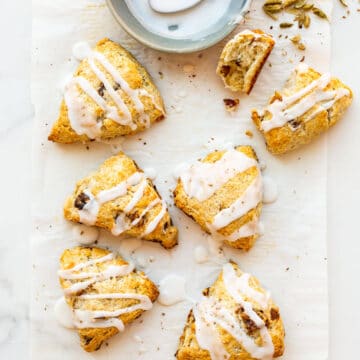 Six (6) glazed fruit scones with icing drizzled on from a bowl with a spoon, sprinkled with freshly ground cardamom from pods