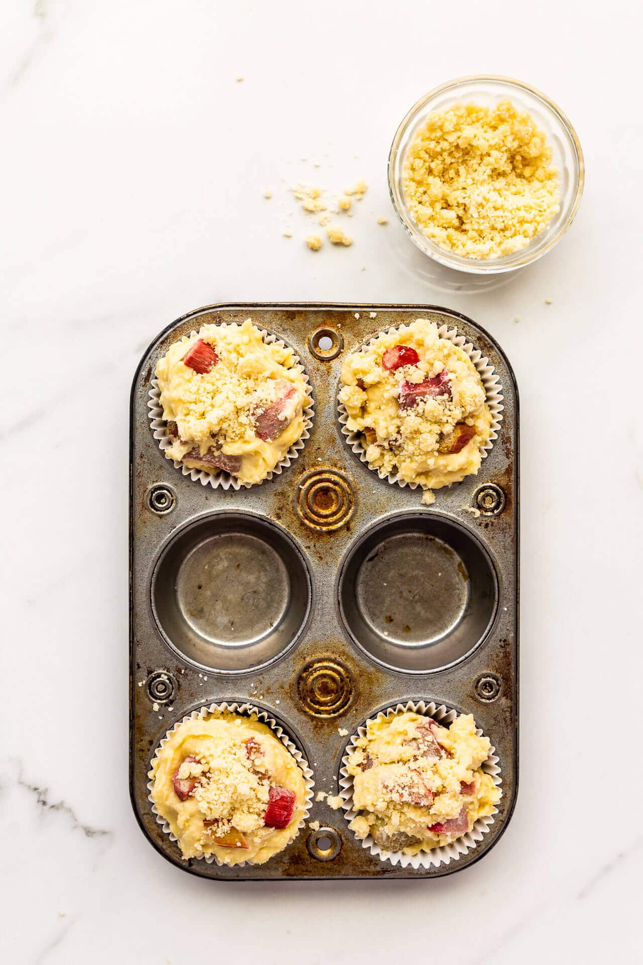 Rhubarb muffins with streusel topping crumbled on top before baking in a vintage muffin pan