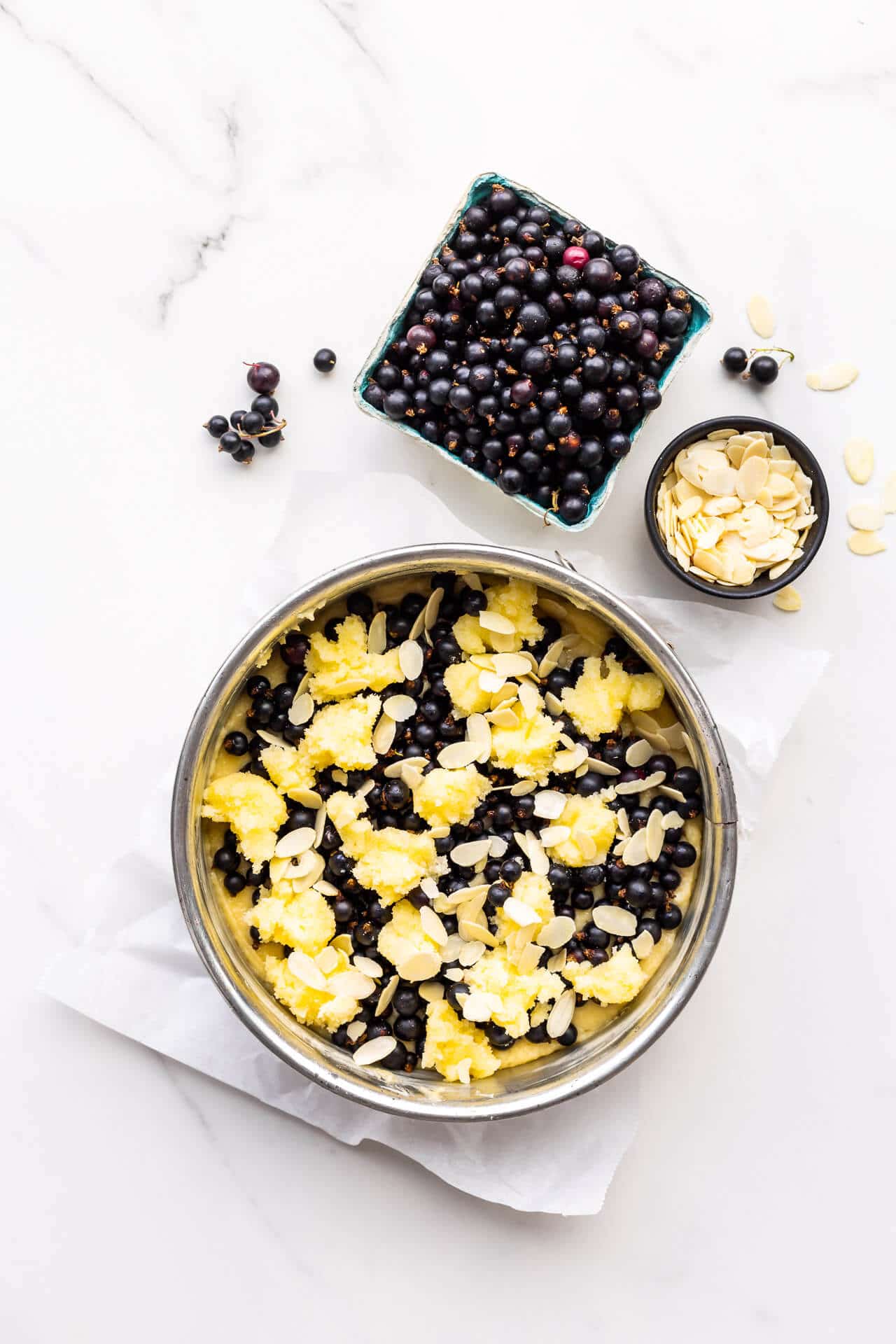 Assembling black currant cake topping cake batter in springform pan with berries, sugar paste, and sliced almonds