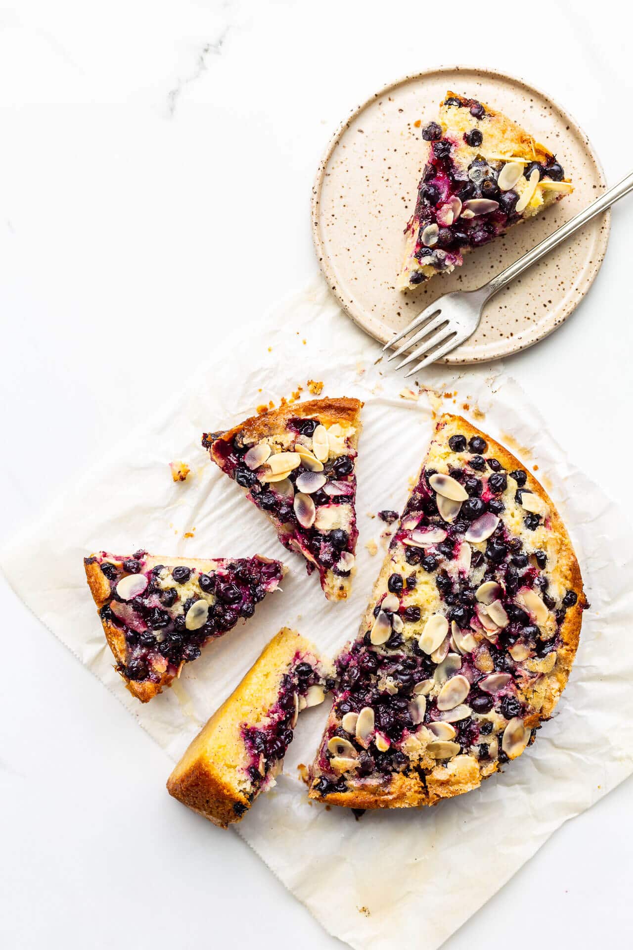 Black currant cake sliced into pieces with one on a speckled ceramic plate with a fork