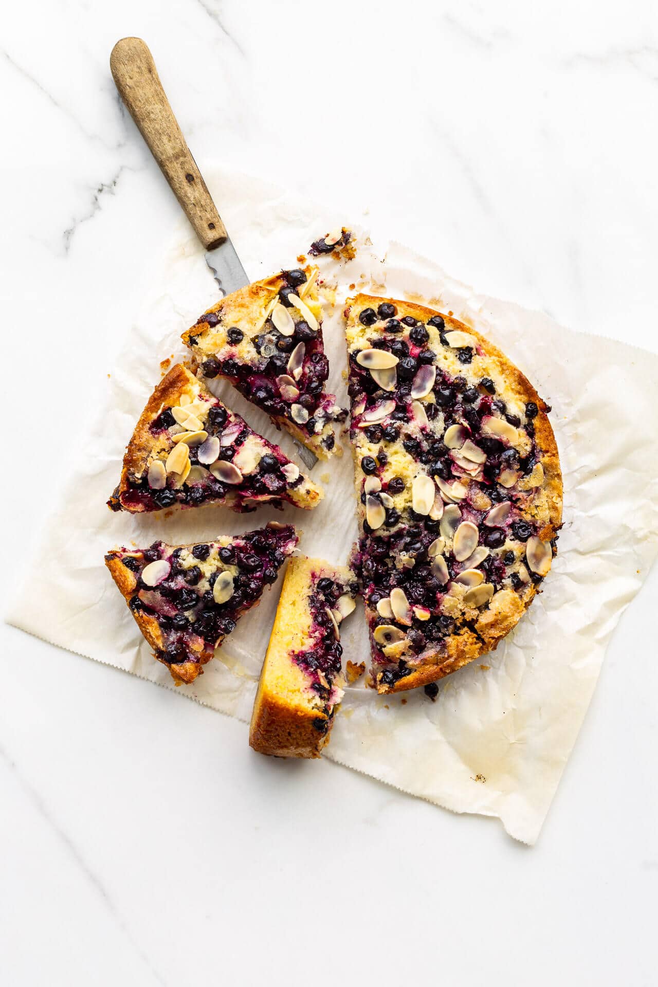 Sliced black currant cake on parchment paper with a wood-handled knife to serve