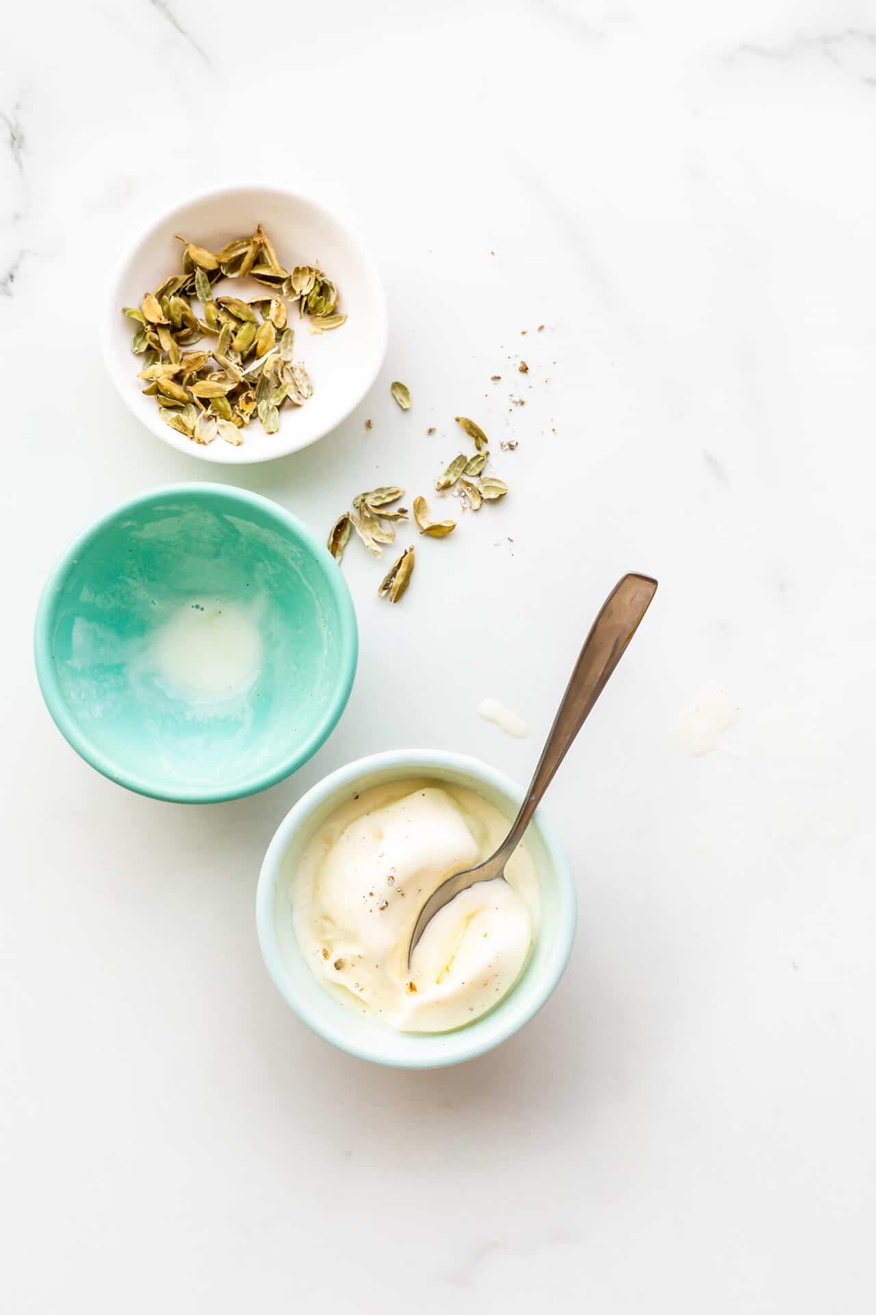 Bowls of cardamom ice cream, one finished, and a small bowl of cardamom pods on the side