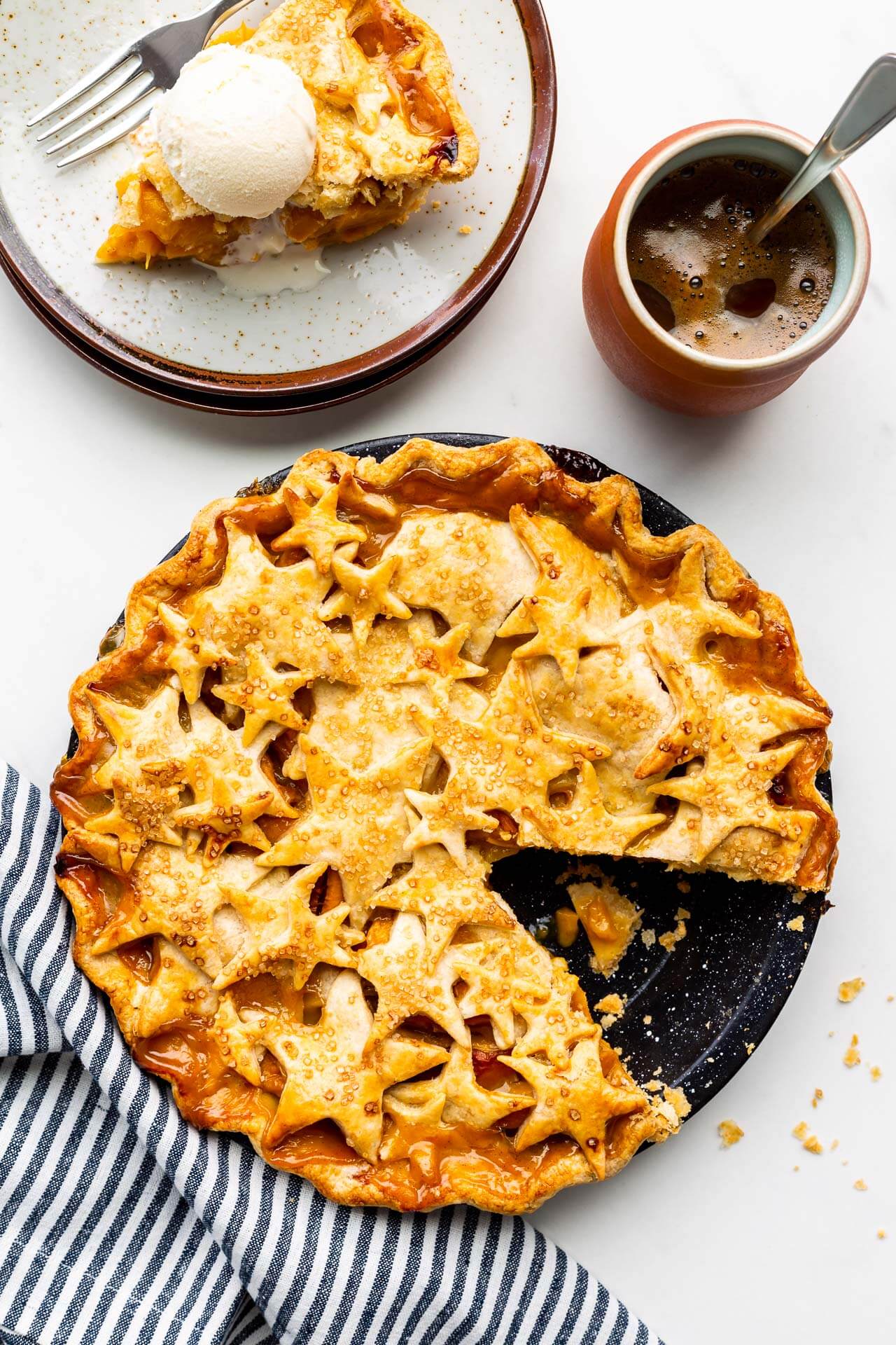 Serving peach mango pie on ceramic plate with cup of coffee (pie has star design on top crust)