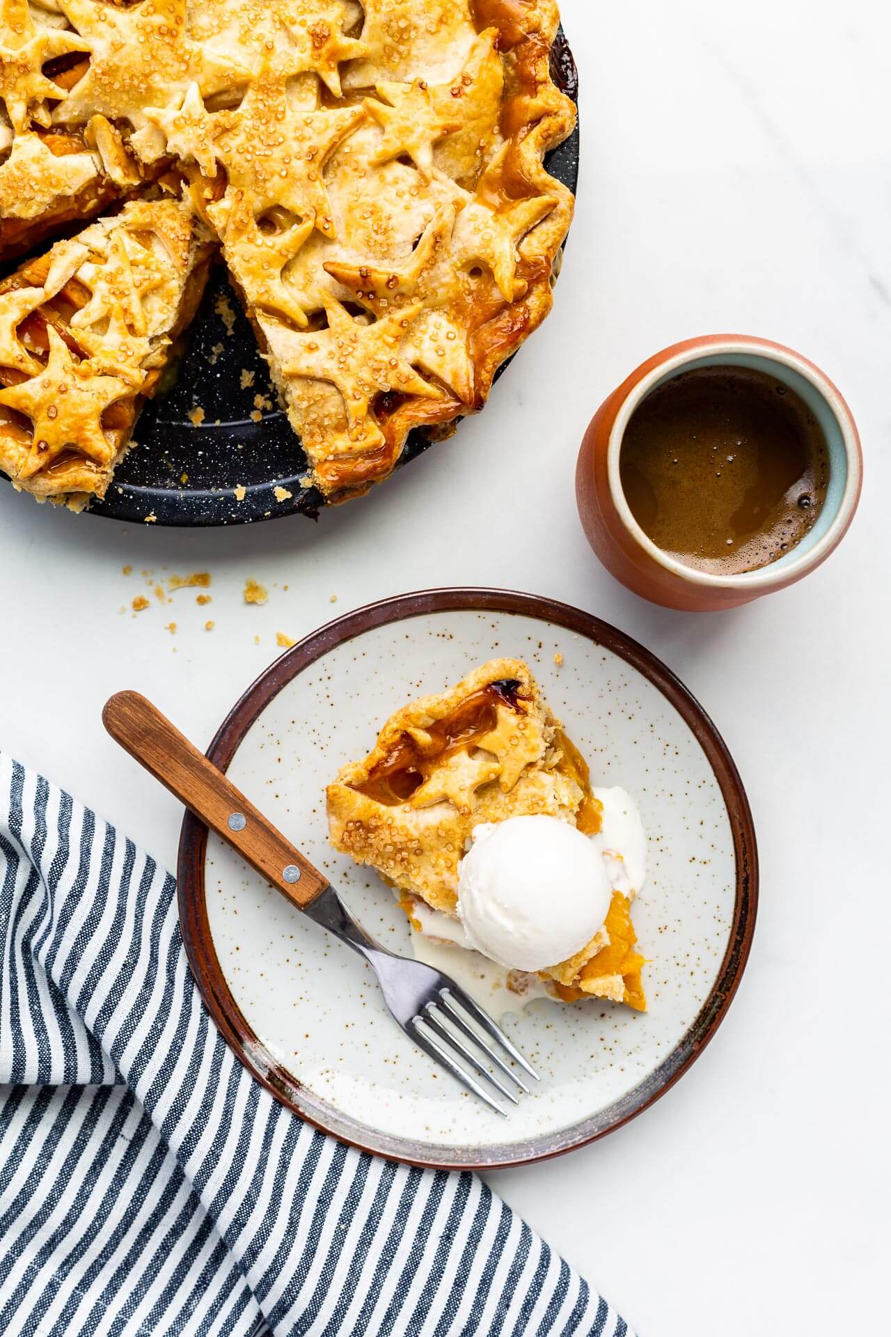 Serving peach mango pie on ceramic plate with cup of coffee (pie has star design on top crust)