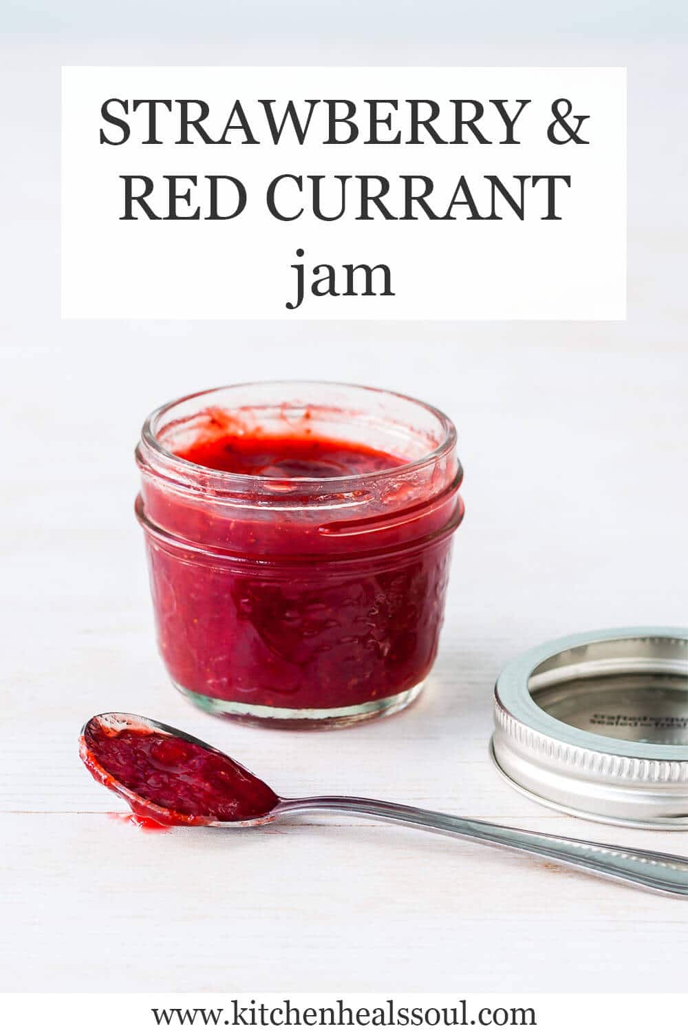 A jar of red currant jam made with strawberries with spoon of jam on side and metal bands