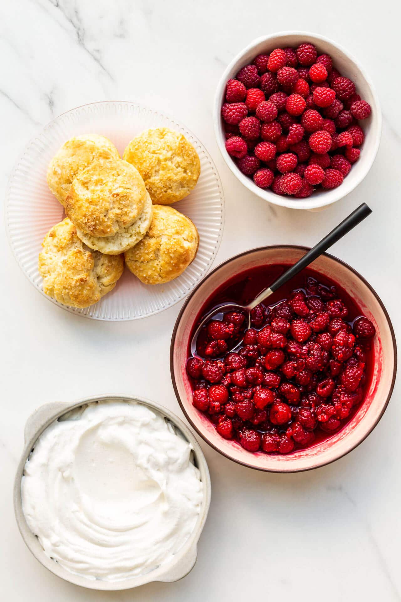 Ingredients to make raspberry shortcake are homemade biscuits, whipped cream, and macerated raspberries