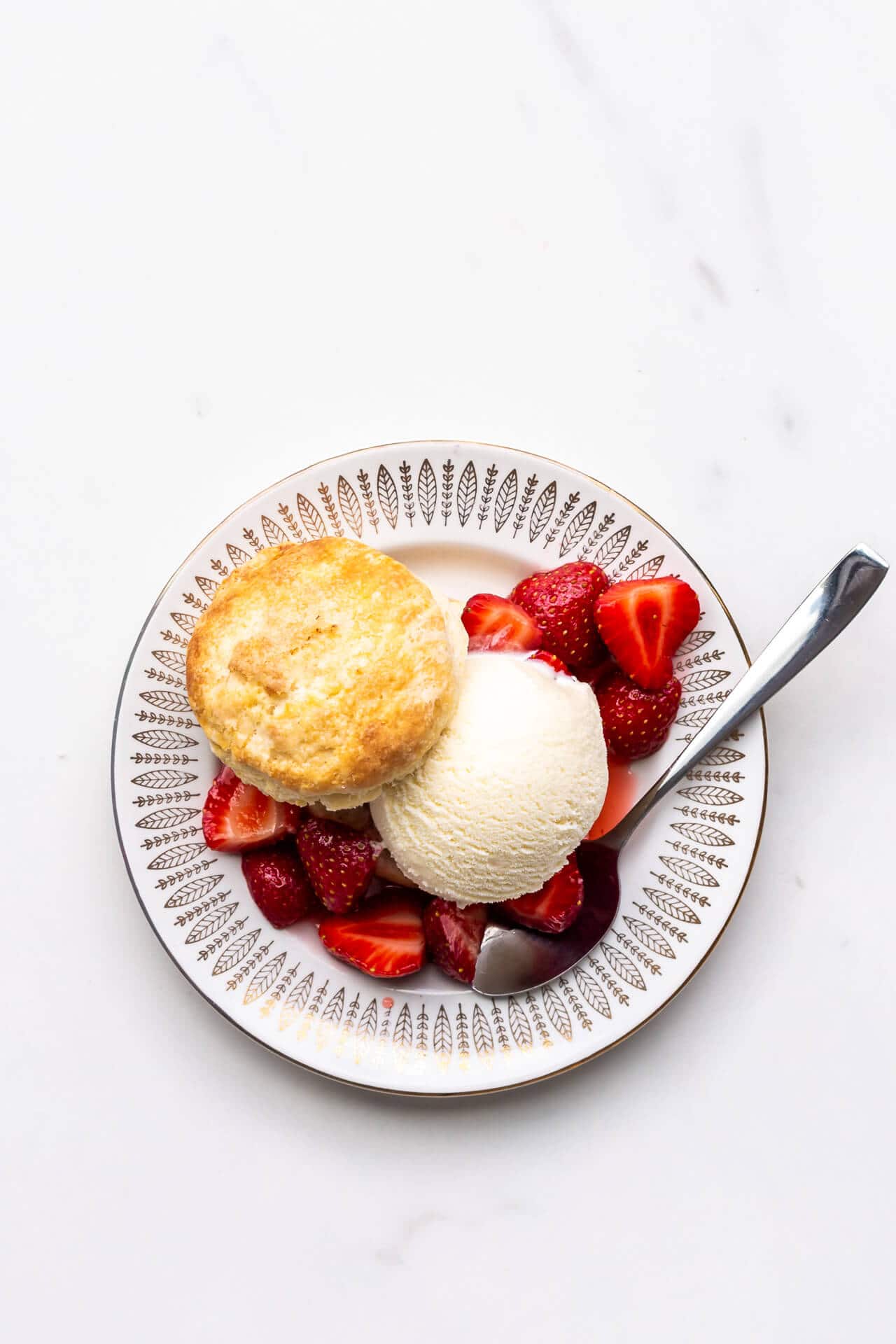 A strawberry shortcake biscuit filled with a scoop of ice cream and fresh strawberries on a small plate