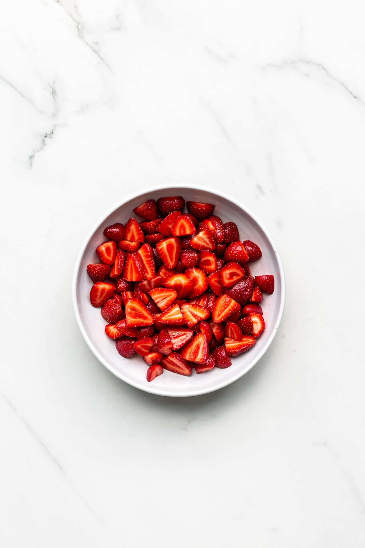 Macerating sliced strawberries with granulated sugar in a bowl to bring out the juices and sweeten them.