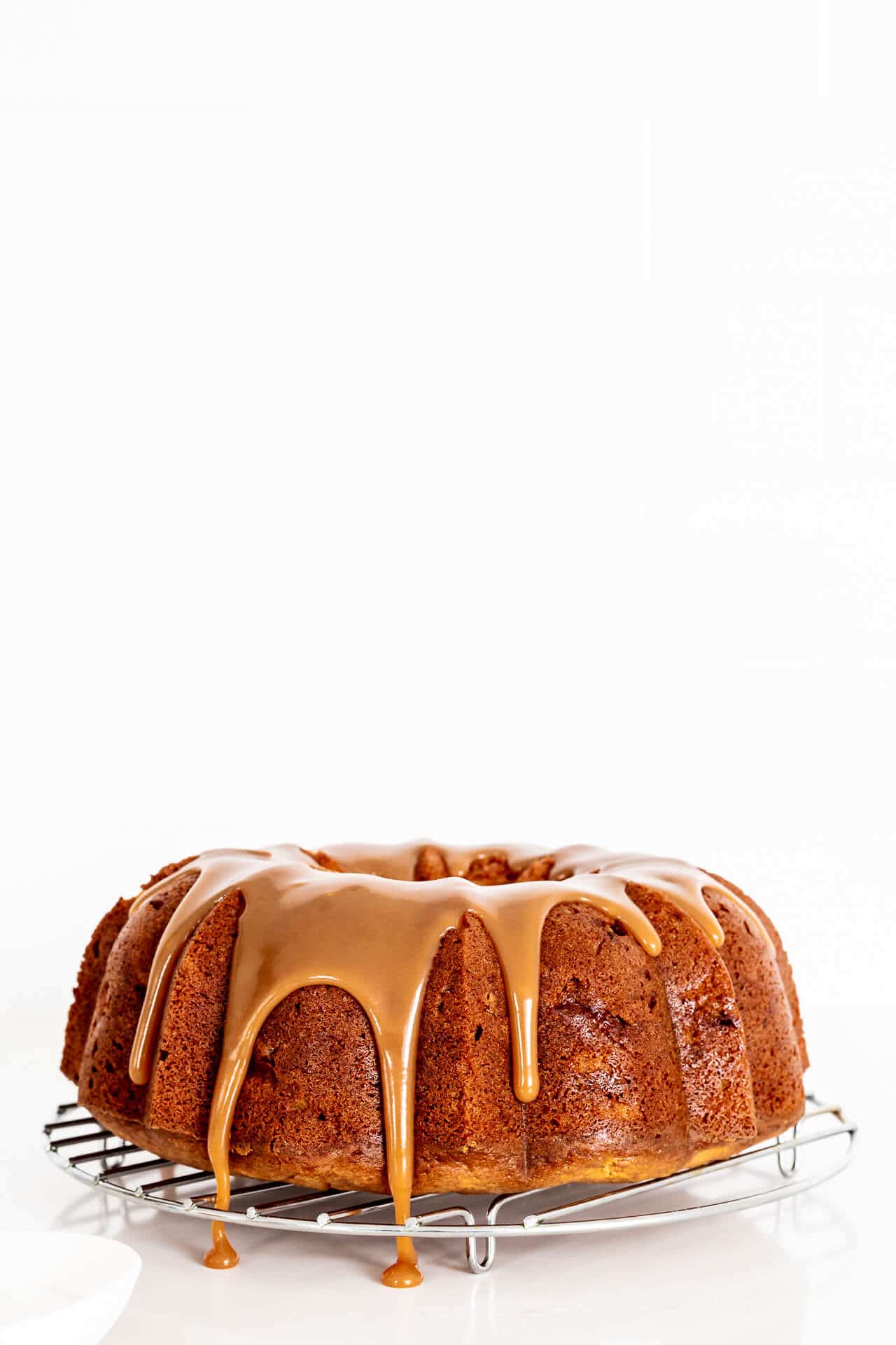 Drizzling salted caramel over a bundt cake set on a wire rack