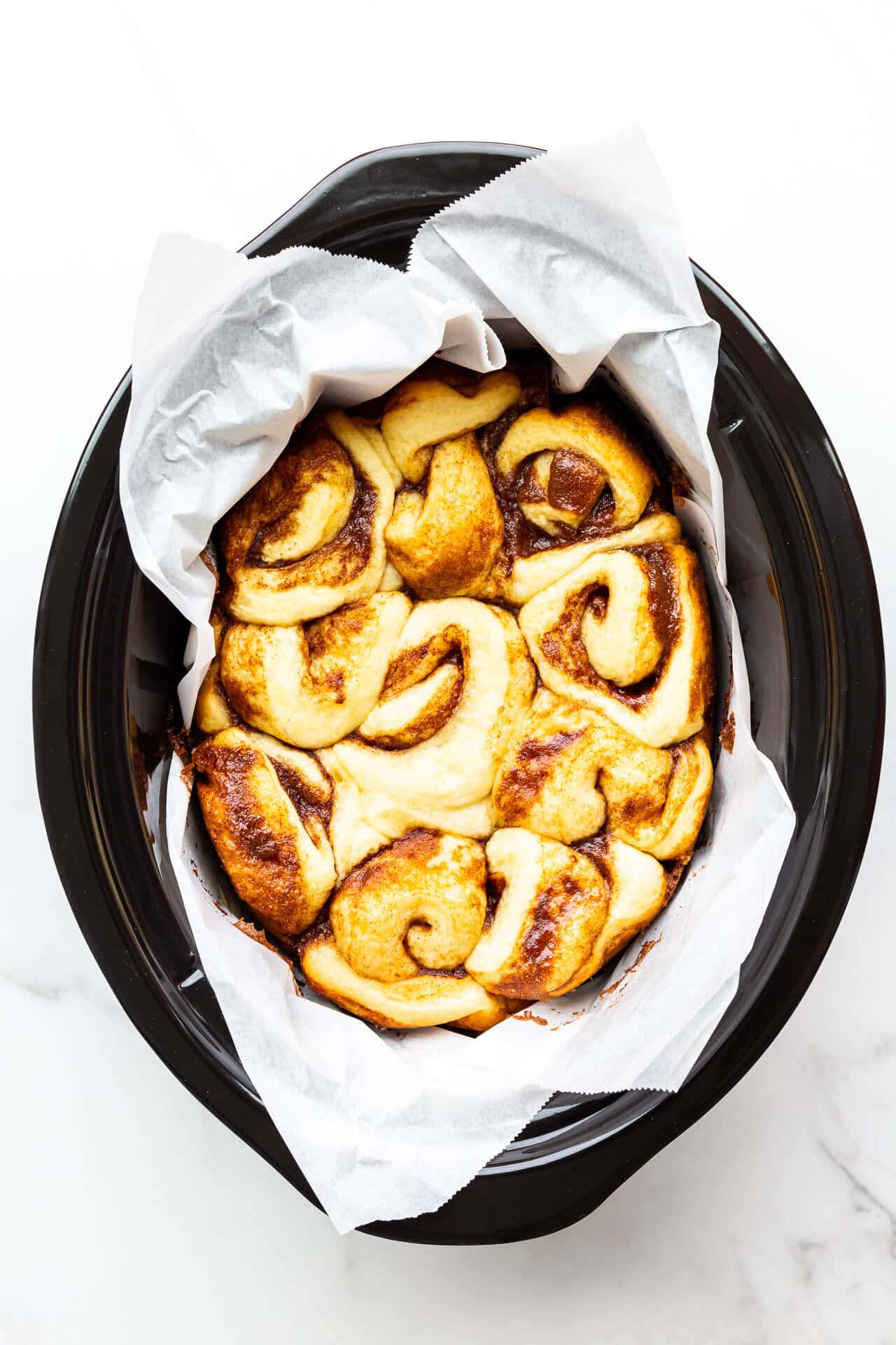 Cinnamon buns baked in a black ceramic slow cooker insert lined with parchment paper