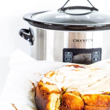 Frosted Crock-Pot cinnamon rolls freshly baked next to the slow cooker they were baked in