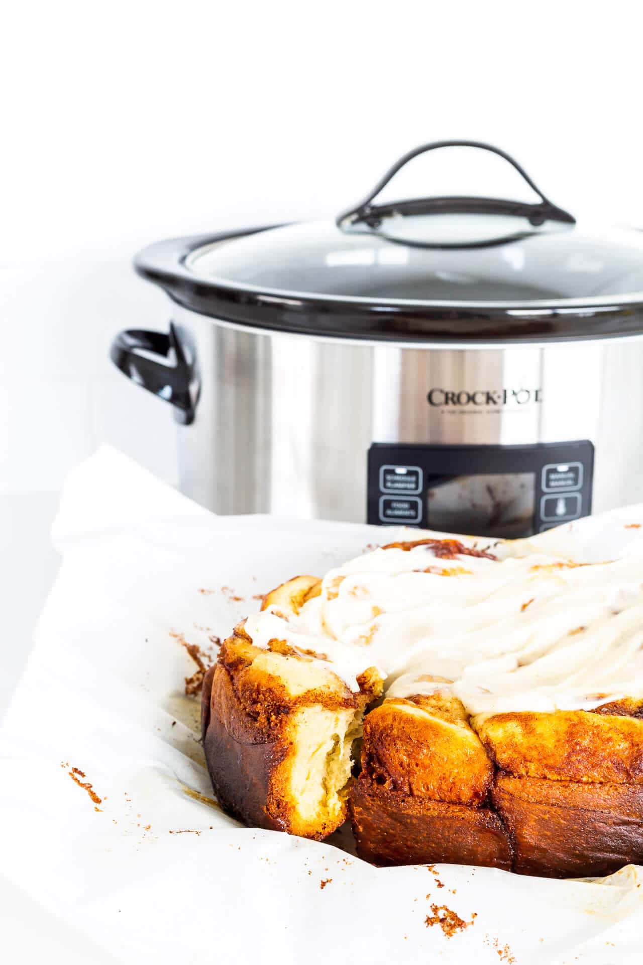 Frosted Crock-Pot cinnamon rolls freshly baked next to the slow cooker they were baked in