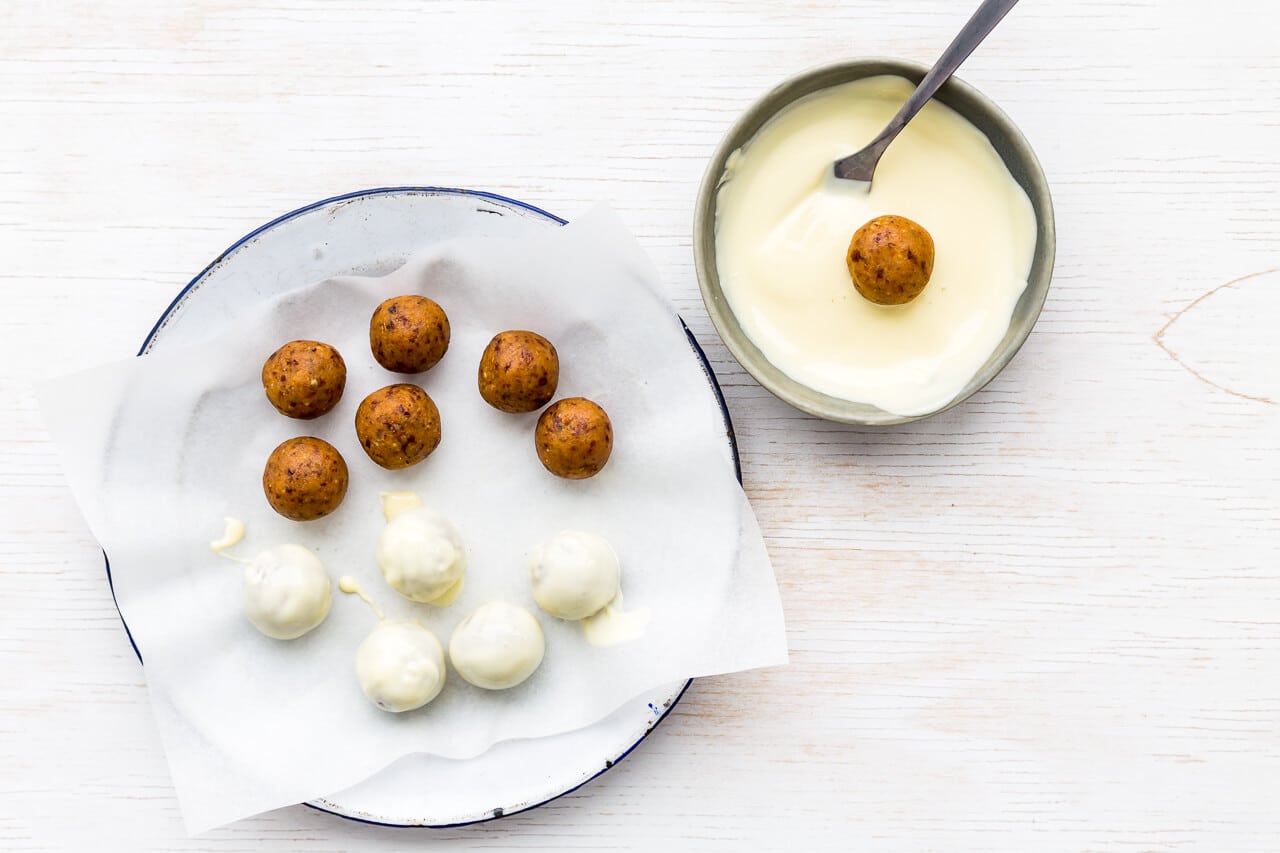 Fruitcake truffles being dipped in a bowl of melted white chocolate to coat them, and set on a plate lined with parchment paper so they don't stick