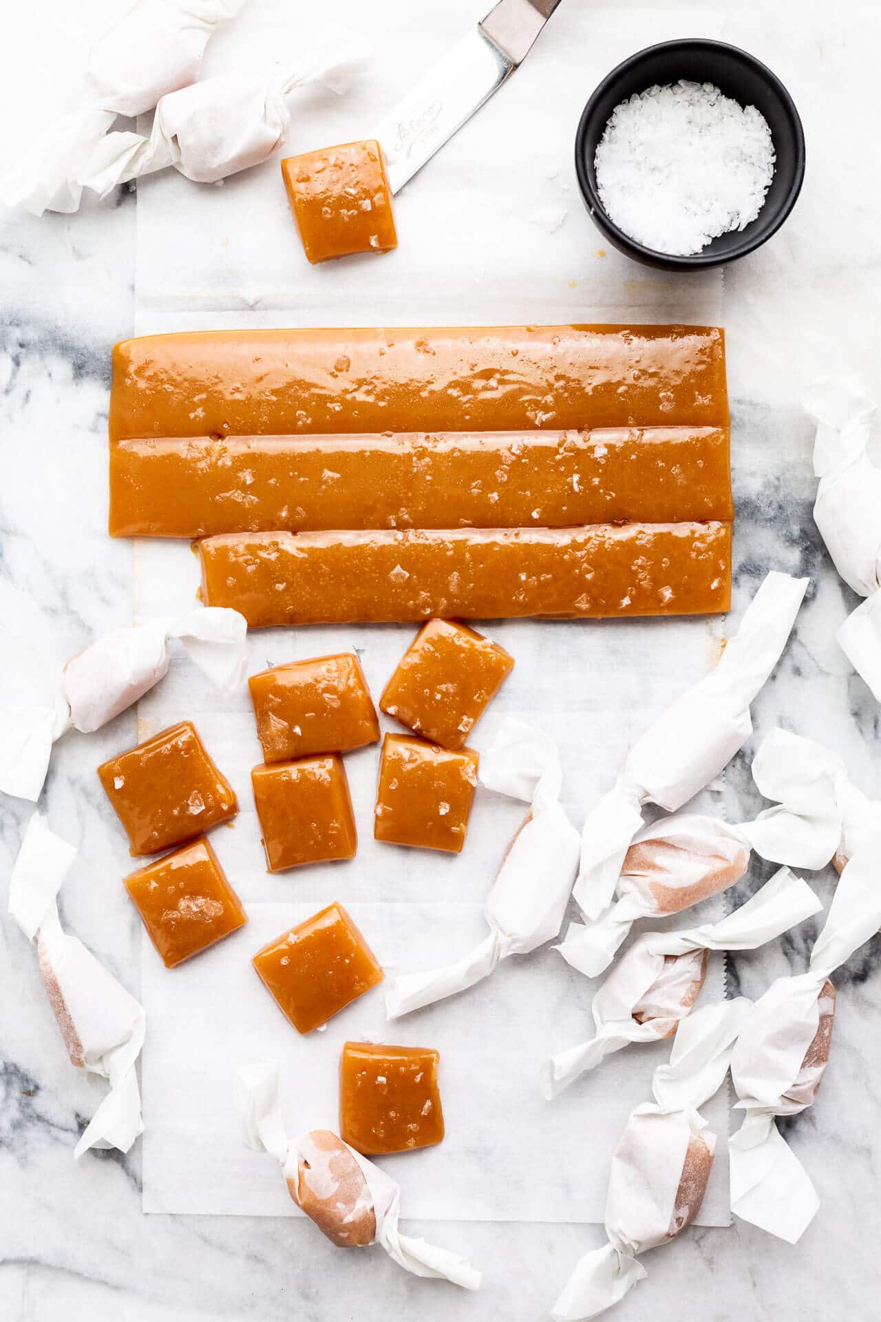 Individually wrapping homemade salted caramels in squares of parchment paper and garnishing with flaky sea salt before wrapping them