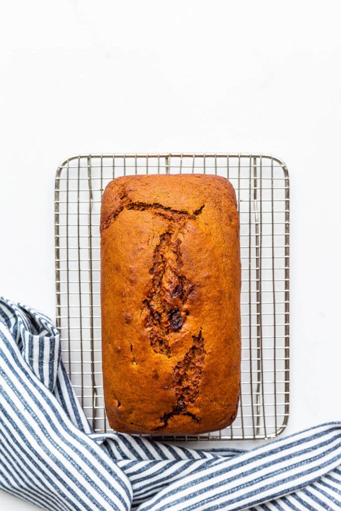 Pumpkin cranberry bread cooling on a wire rack with a striped linen