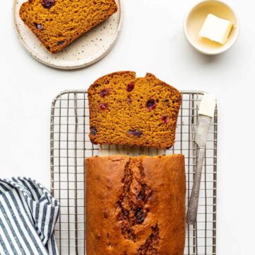 Sliced pumpkin cranberry bread on cooling rack being served with butter