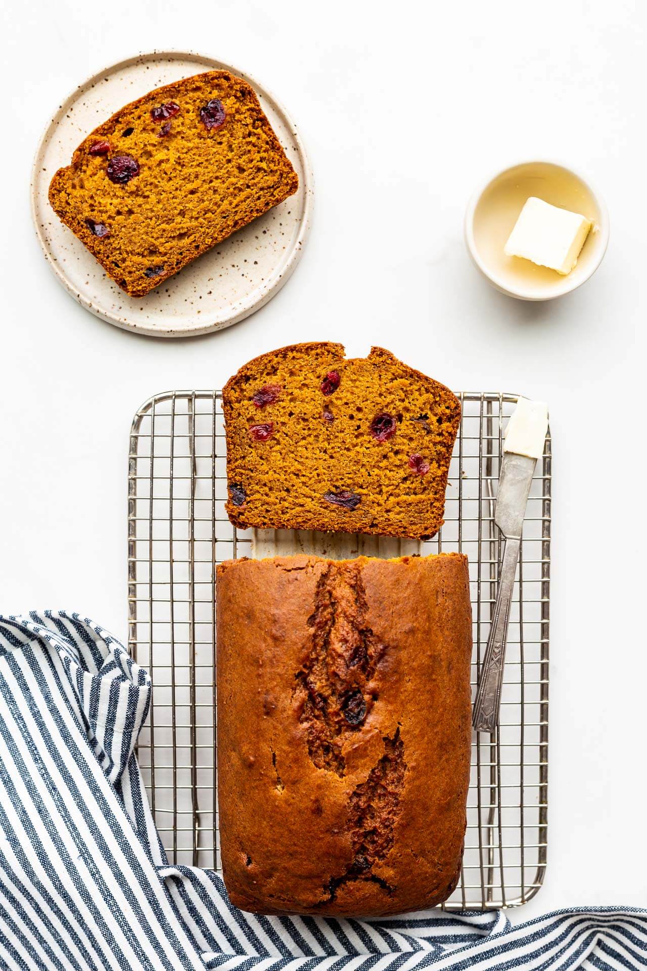 Sliced pumpkin cranberry bread on cooling rack being served with butter