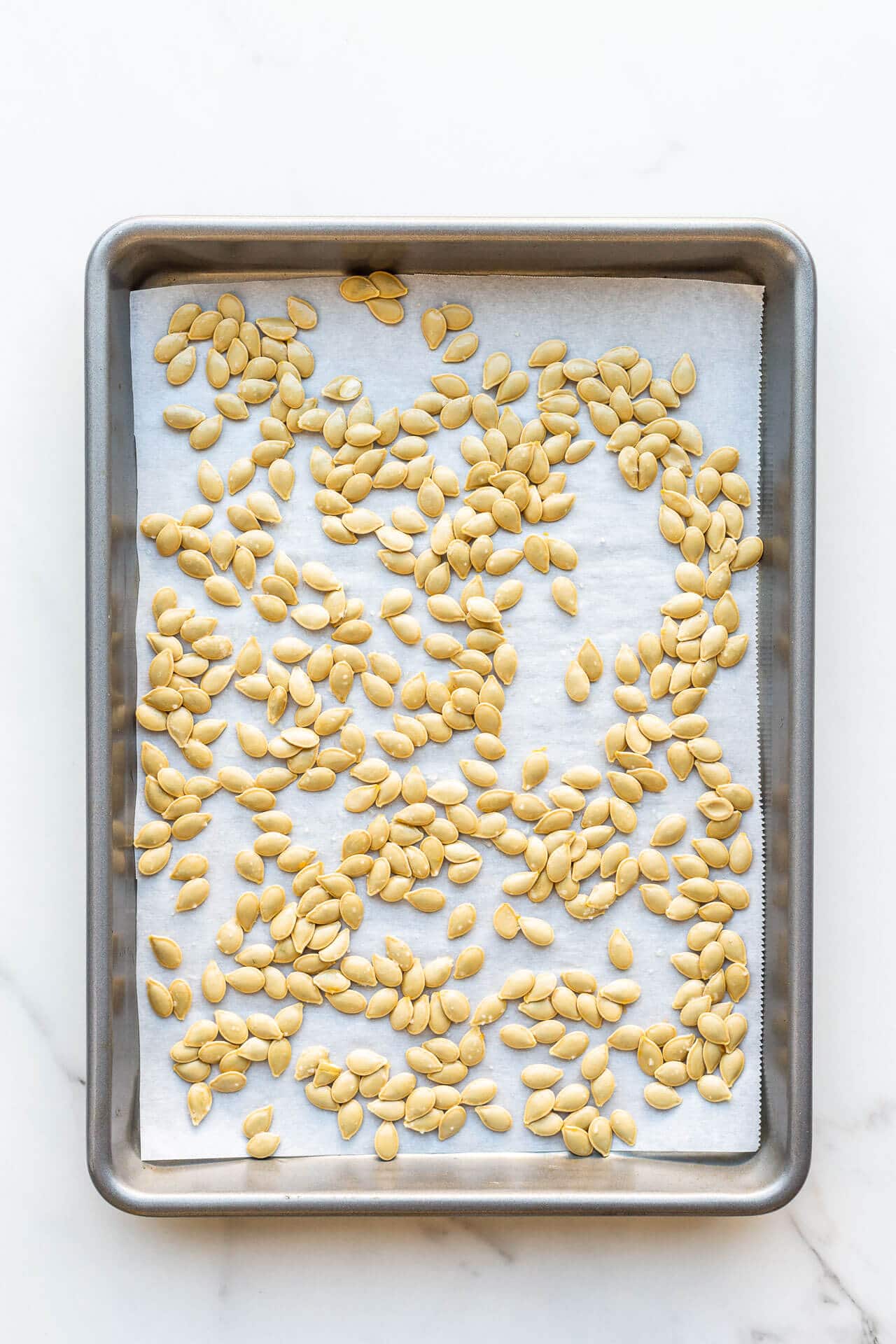 Pumpkin seeds on a sheet pan lined with parchment ready to be toasted in the oven