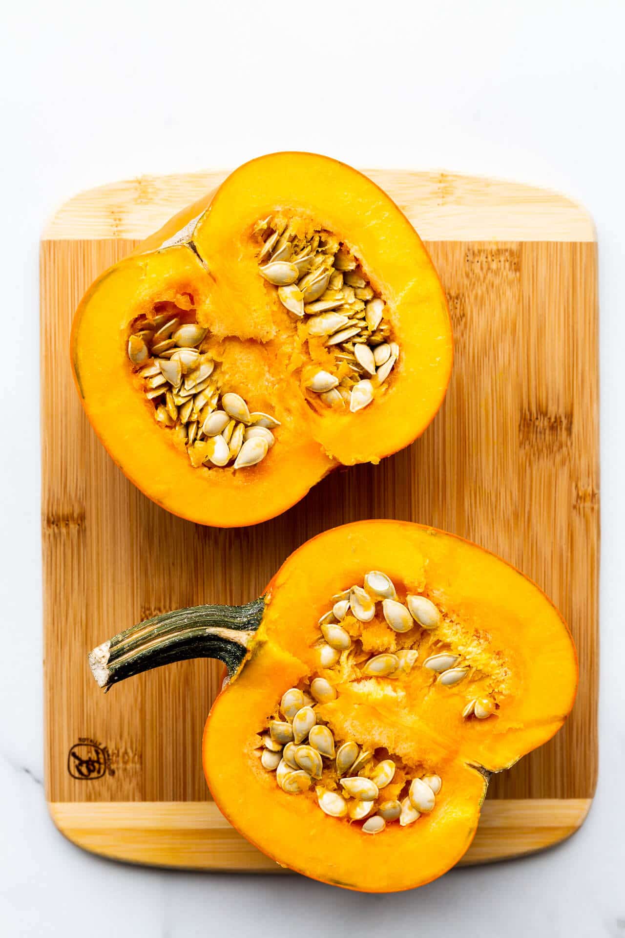 Sugar pie pumpkin cut in half to reveal flesh and seeds on a wood cutting board.