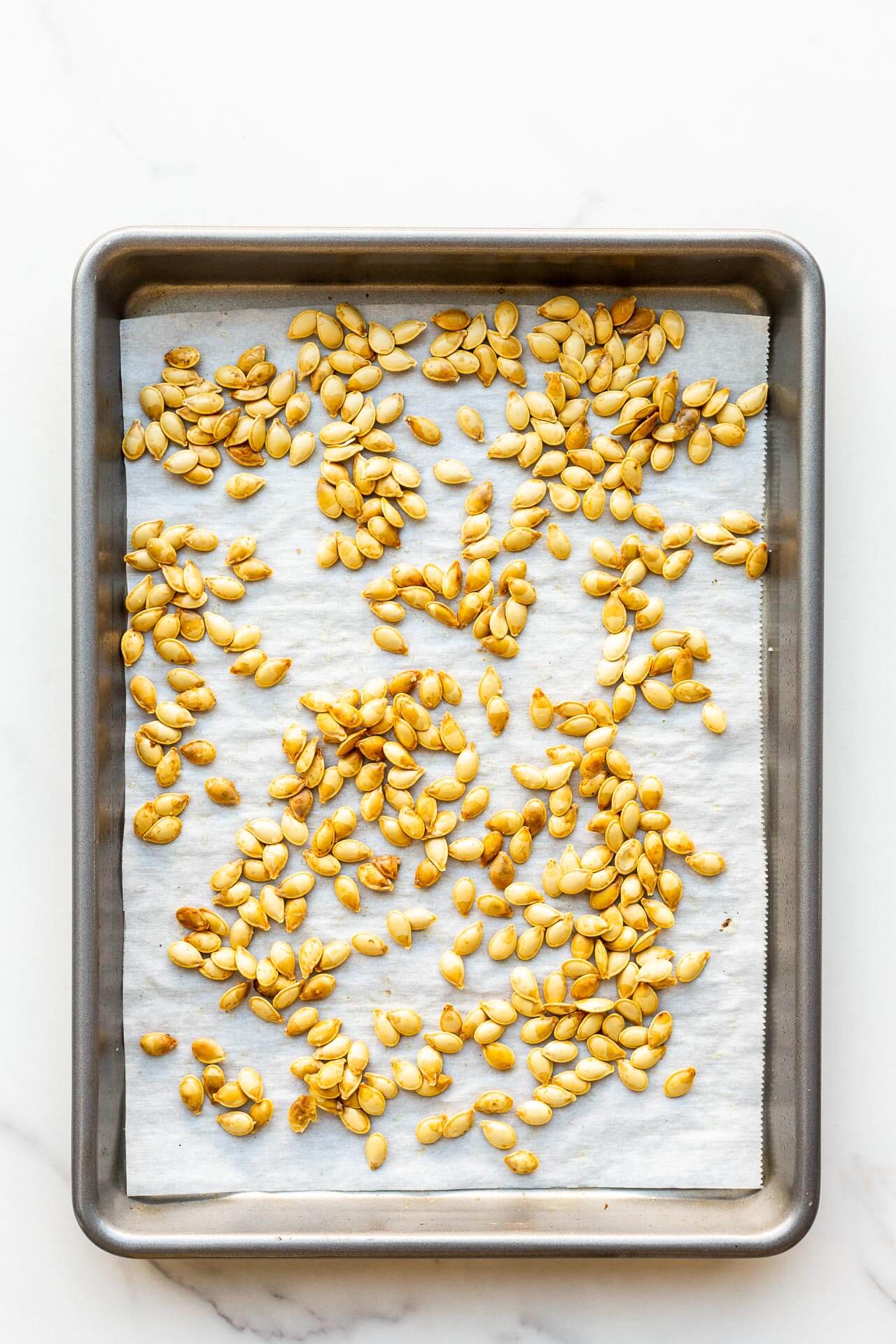 Pumpkin seeds toasted on a sheet pan lined with parchment paper.