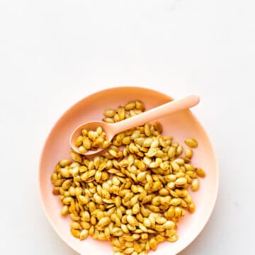 A pink bowl of toasted pumpkin seeds with a pink spoon for serving