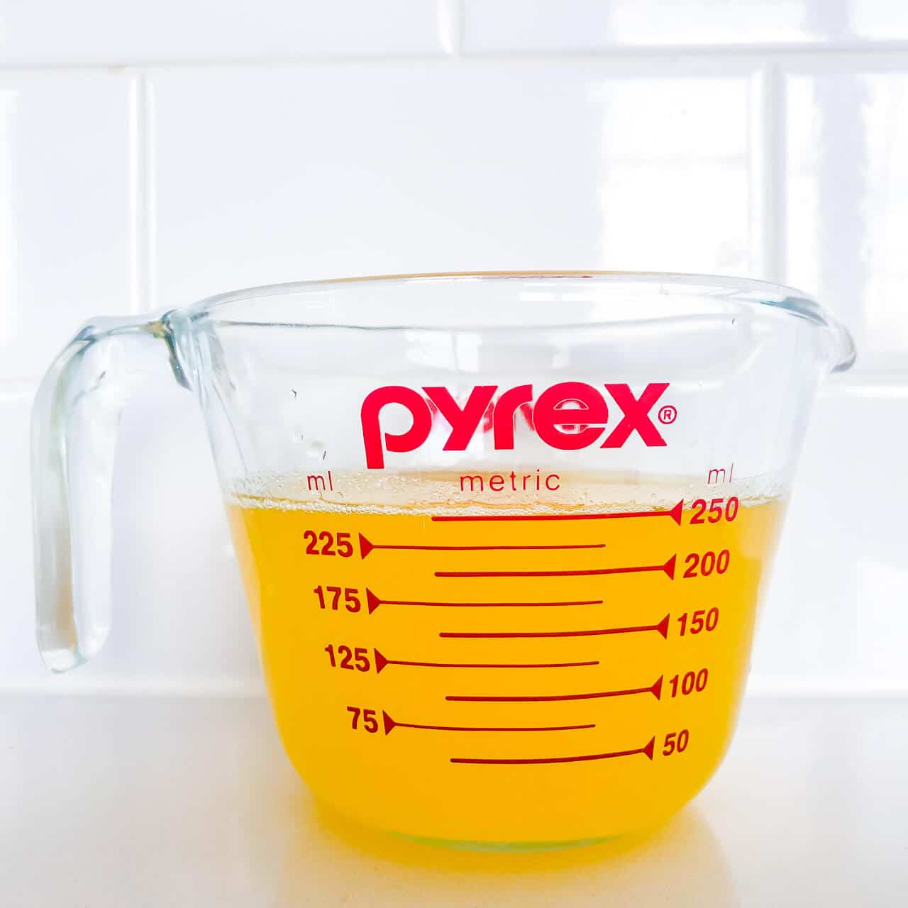 Warm clarified butter in a measuring cup is golden in colour and fluid.