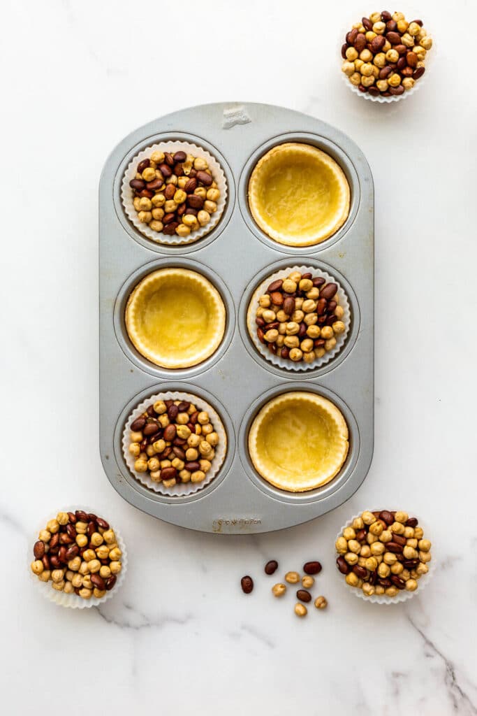 Blind baking tart shells in a muffin pan, using silicone muffin liners and dried beans to weigh down the crust.