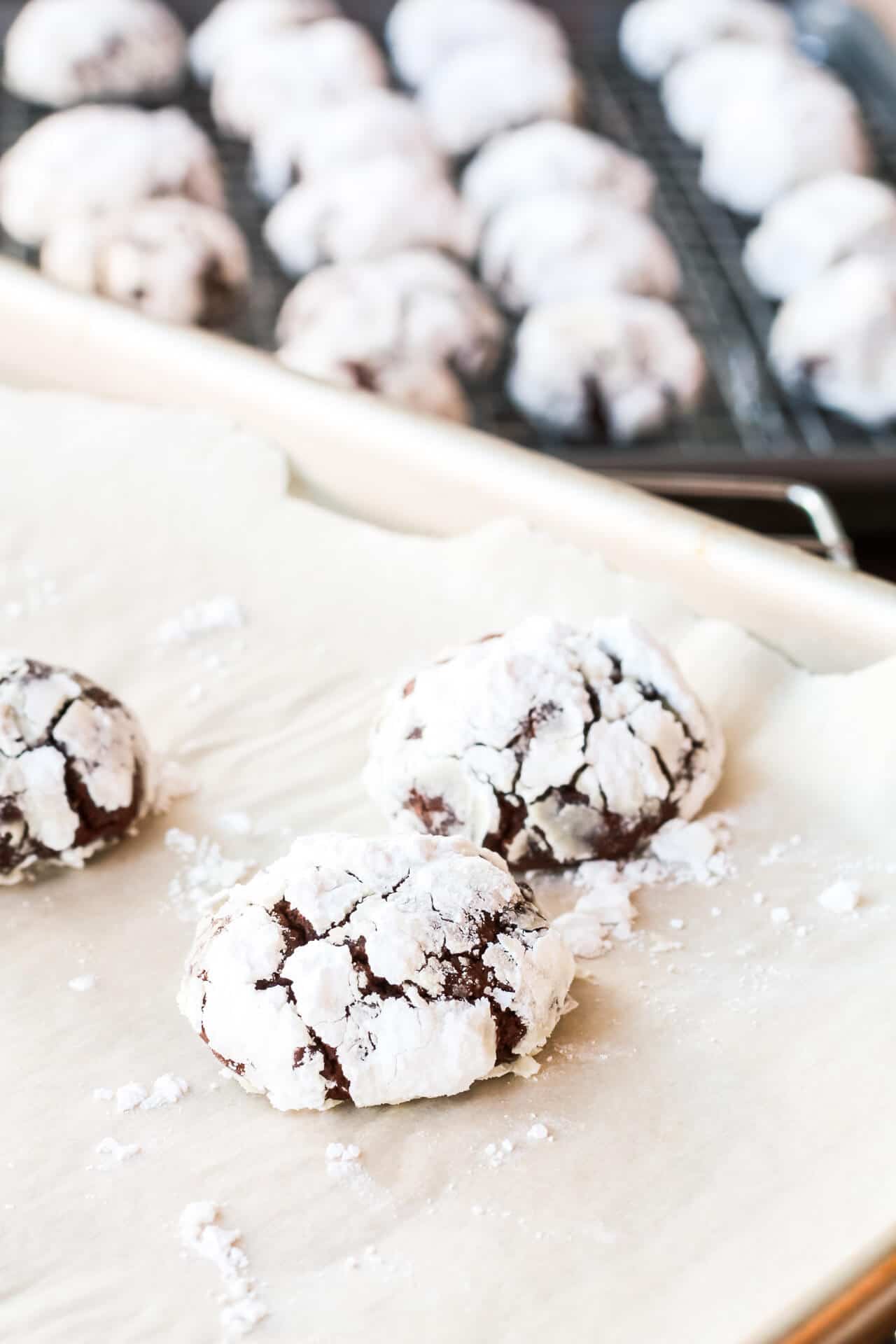 A sheet pan with baked chocolate crinkle cookies to be transferred to a cooling rack in the background.