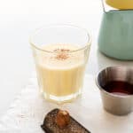 A small glass of eggnog topped with freshly grated nutmeg and a shot of rum to mix into it.