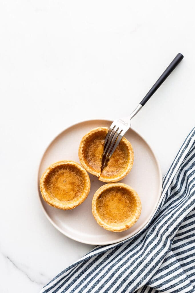 A beige plate with three butter tarts on it and a fork cutting open one of them.