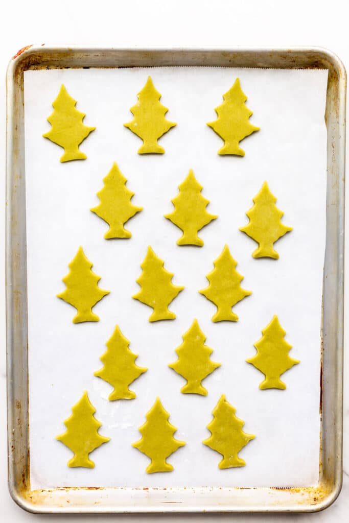 Matcha cookies cutout in tree shapes on a sheet pan lined with parchment paper.