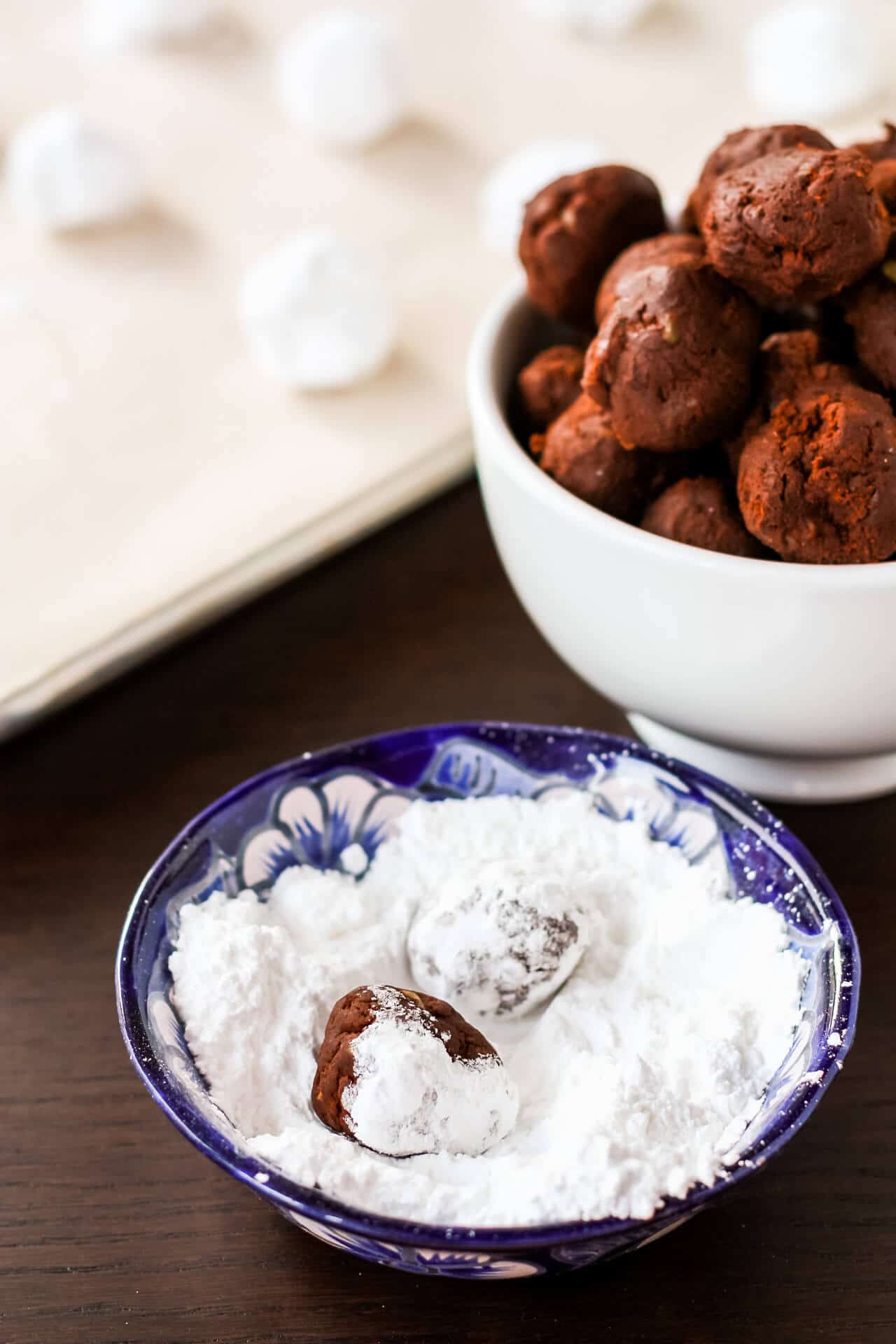 Rolling scoops of chocolate cookie dough in powdered sugar to make crackle cookies.