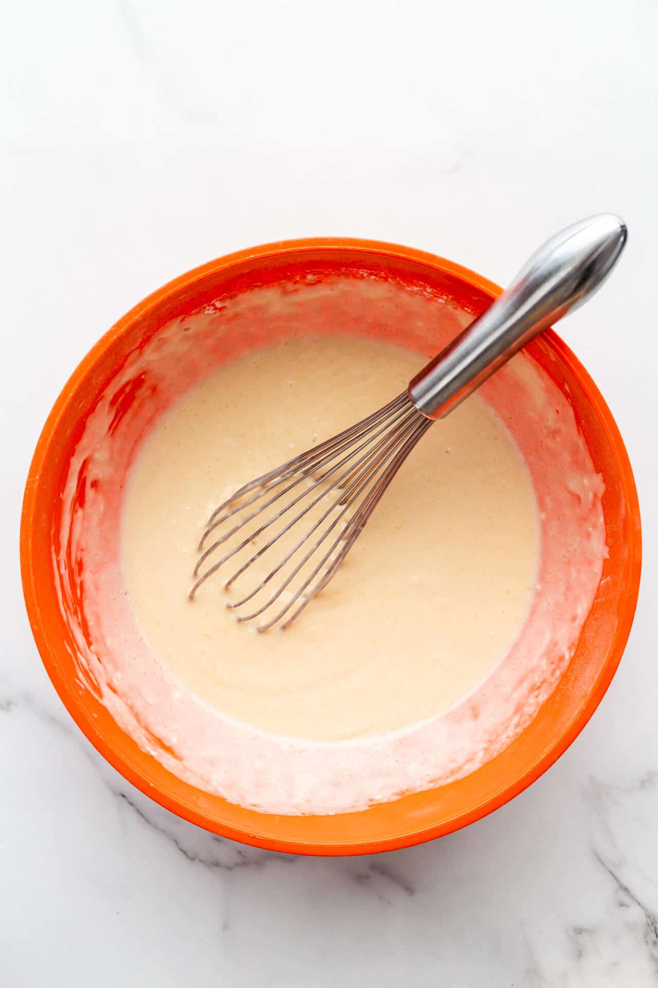 Waffle batter mixed with a whisk in an orange bowl.