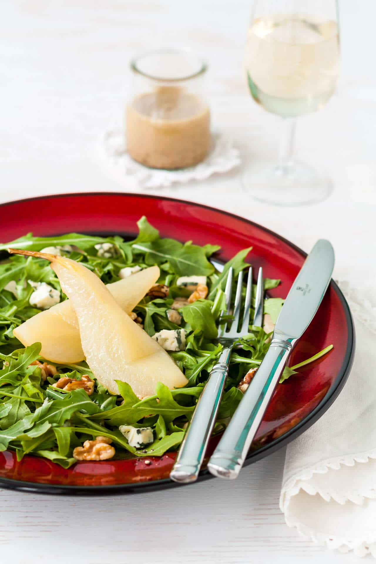 A salad of poached pears on a bed of arugula with blue cheese and walnuts on a red plate.