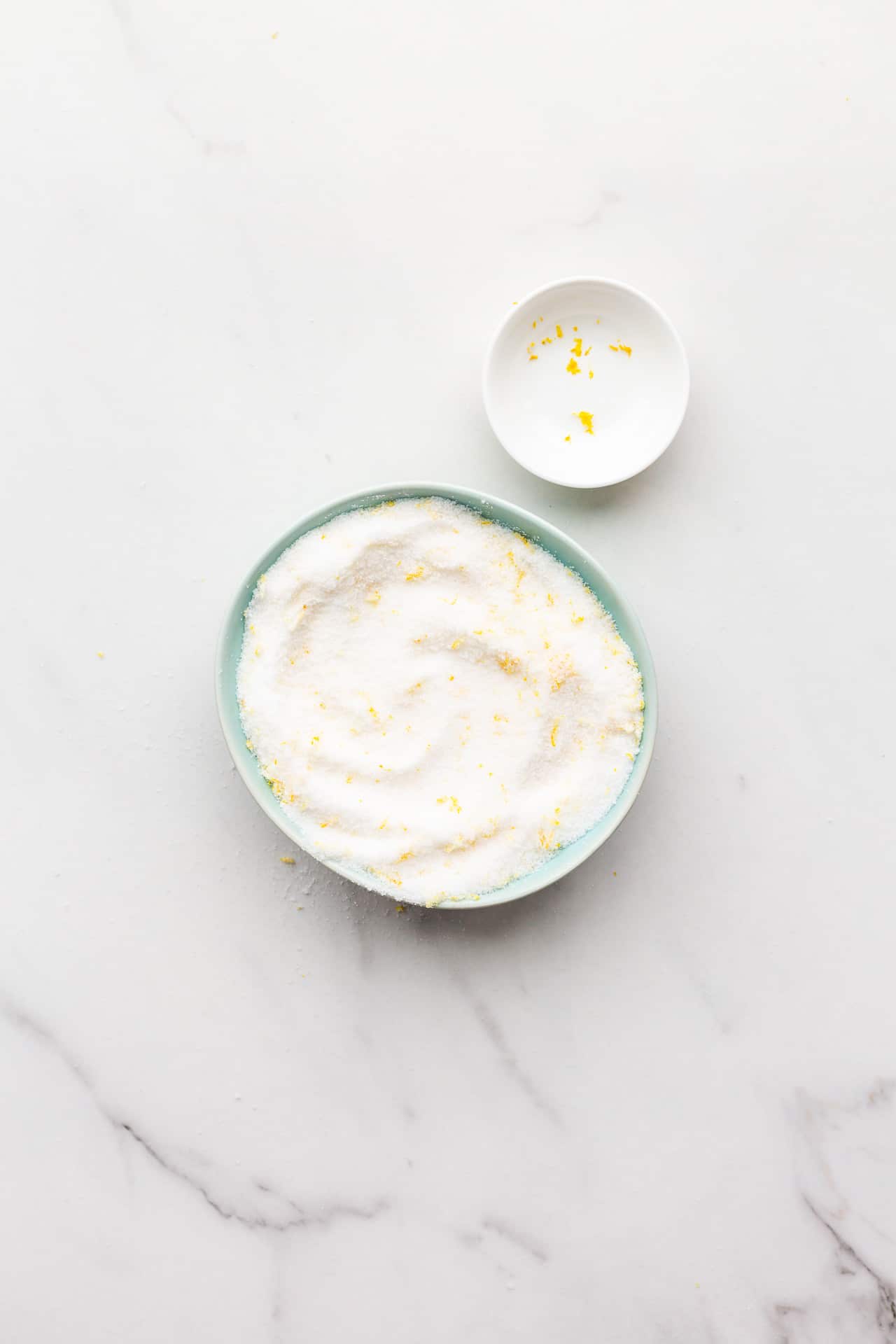 A bowl of freshly made lemon sugar near a small pinch bowl that has a few leftover strands of lemon zest.