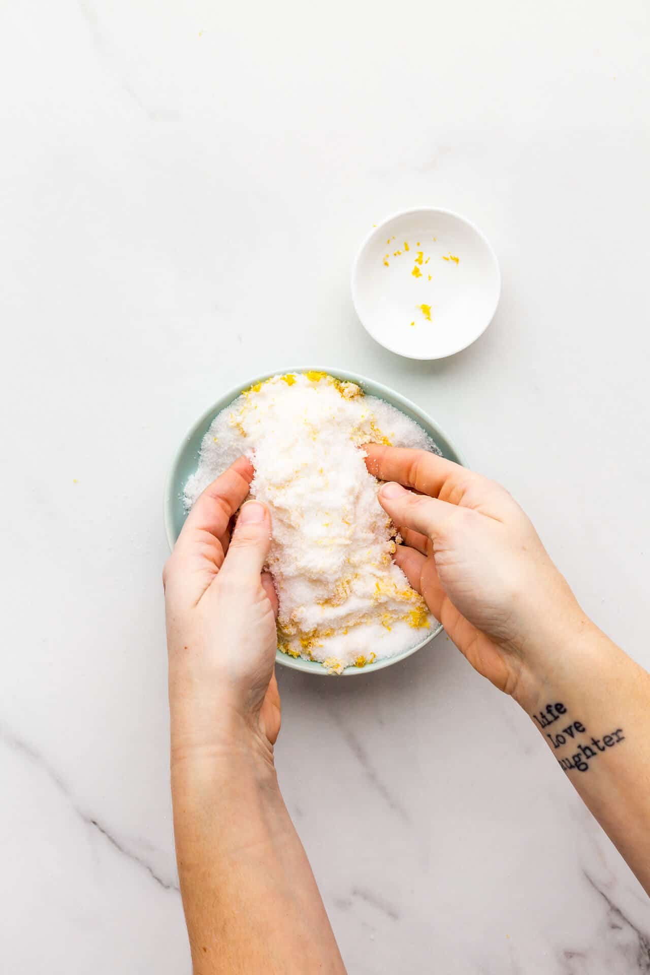 Rubbing together lemon zest and sugar to make lemon sugar in a small bowl.