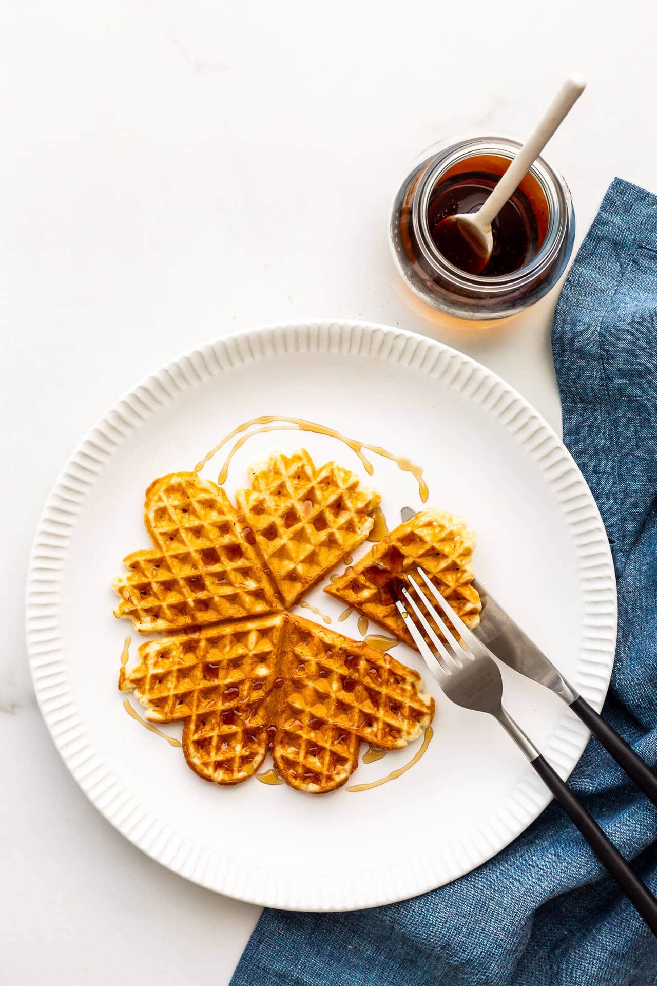 Waffle on a white plate with maple syrup and a blue linen napkin.