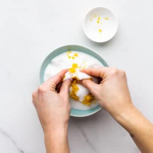 Rubbing lemon zest into granulated sugar in a bowl to make lemon sugar.