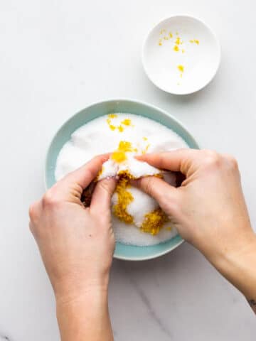Rubbing lemon zest into granulated sugar in a bowl to make lemon sugar.
