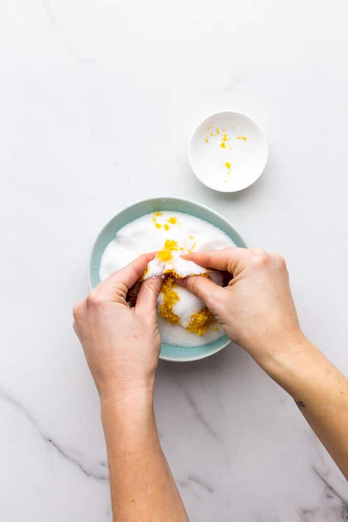 Rubbing lemon zest into granulated sugar with fingertips in a bowl to make lemon sugar.