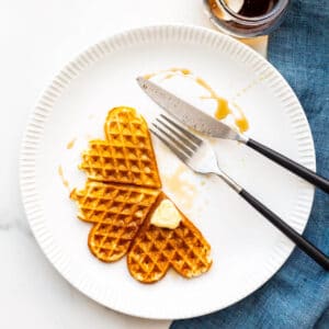 Waffles on a plate with maple syrup and a pat of butter.